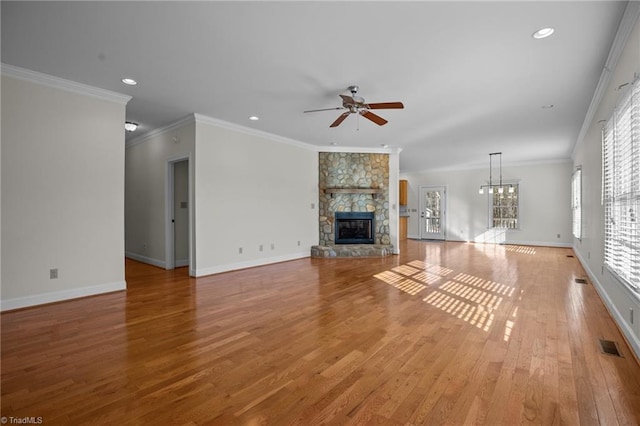 unfurnished living room with ceiling fan with notable chandelier, a fireplace, ornamental molding, and light wood-type flooring