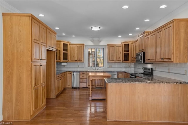 kitchen with appliances with stainless steel finishes, tasteful backsplash, dark hardwood / wood-style flooring, ornamental molding, and kitchen peninsula