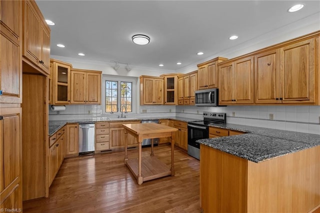 kitchen featuring sink, appliances with stainless steel finishes, wood-type flooring, kitchen peninsula, and dark stone counters