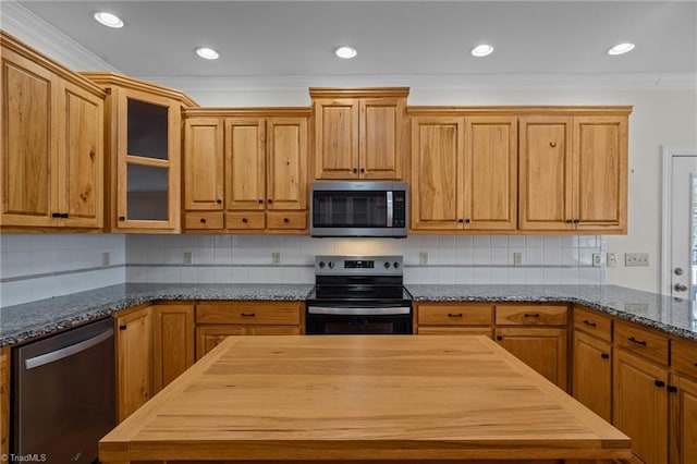 kitchen with dark stone countertops, decorative backsplash, ornamental molding, and stainless steel appliances