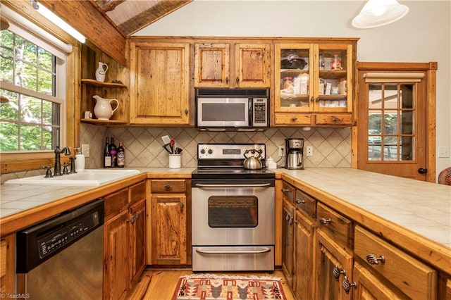 kitchen with light hardwood / wood-style floors, tile countertops, sink, tasteful backsplash, and appliances with stainless steel finishes