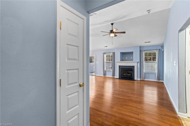 unfurnished living room with baseboards, a fireplace with flush hearth, wood finished floors, a textured wall, and a ceiling fan