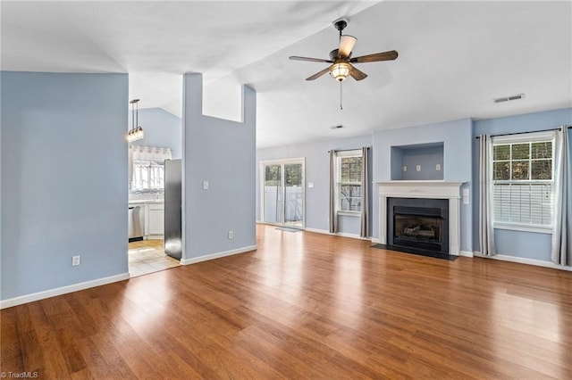 unfurnished living room featuring visible vents, a fireplace with flush hearth, a ceiling fan, wood finished floors, and vaulted ceiling