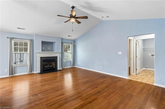 unfurnished living room featuring a fireplace with flush hearth, ceiling fan, visible vents, and wood finished floors