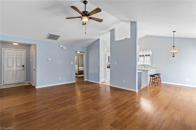 unfurnished living room featuring visible vents, baseboards, vaulted ceiling, ceiling fan with notable chandelier, and wood finished floors