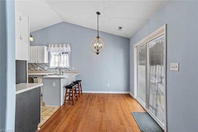 kitchen featuring a breakfast bar, light countertops, vaulted ceiling, a peninsula, and a sink