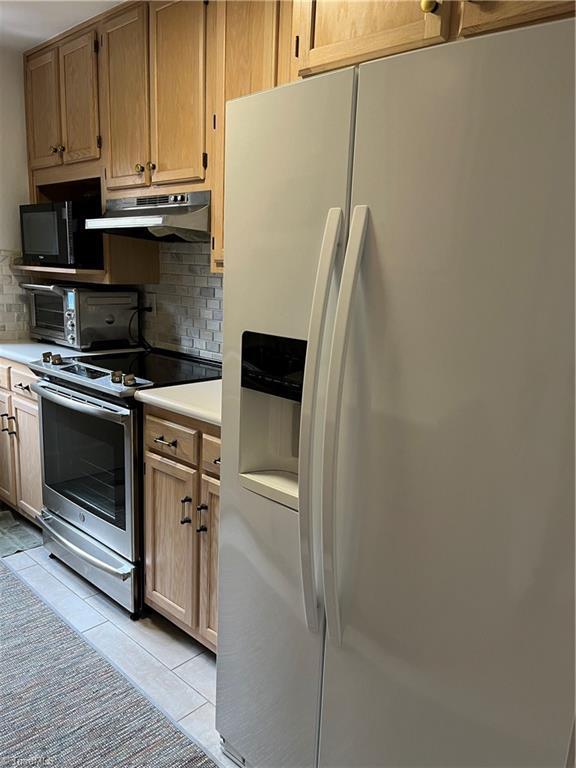 kitchen with backsplash, exhaust hood, refrigerator with ice dispenser, and electric stove