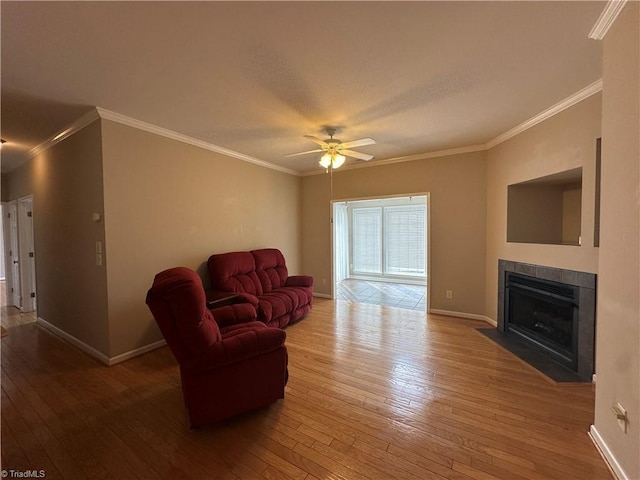 living area with ornamental molding, hardwood / wood-style floors, a tile fireplace, and baseboards