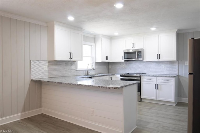 kitchen featuring kitchen peninsula, light stone counters, white cabinets, and appliances with stainless steel finishes