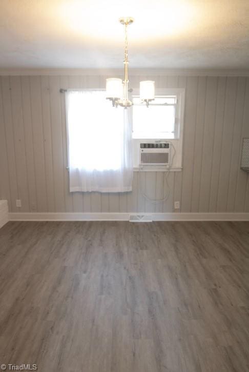 empty room featuring hardwood / wood-style floors, cooling unit, a notable chandelier, and ornamental molding