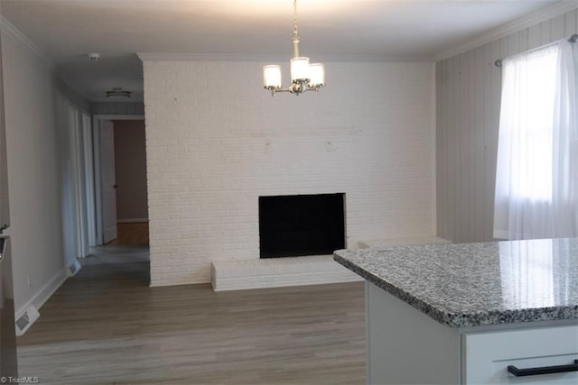 kitchen featuring crown molding, wood-type flooring, pendant lighting, white cabinetry, and a brick fireplace