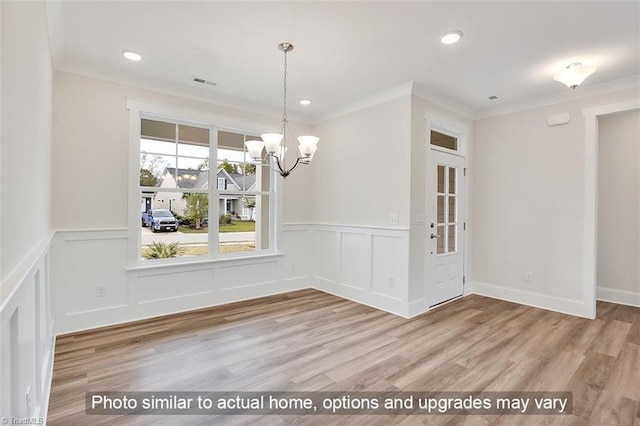unfurnished dining area with a chandelier, a wainscoted wall, ornamental molding, wood finished floors, and a decorative wall