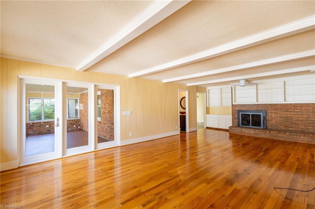 unfurnished living room with a textured ceiling, a brick fireplace, beam ceiling, and hardwood / wood-style floors