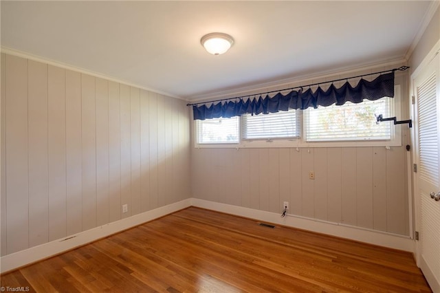 spare room featuring wood-type flooring, wood walls, and crown molding