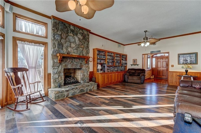 living room with a textured ceiling, a stone fireplace, wood-type flooring, and crown molding