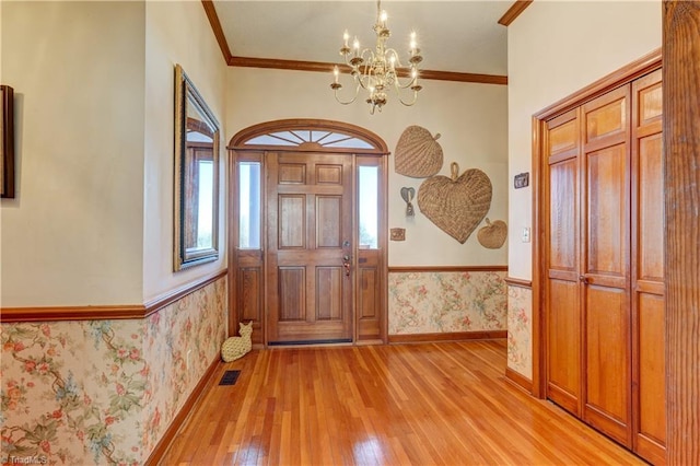 entrance foyer with a notable chandelier, light wood-type flooring, ornamental molding, and a wealth of natural light