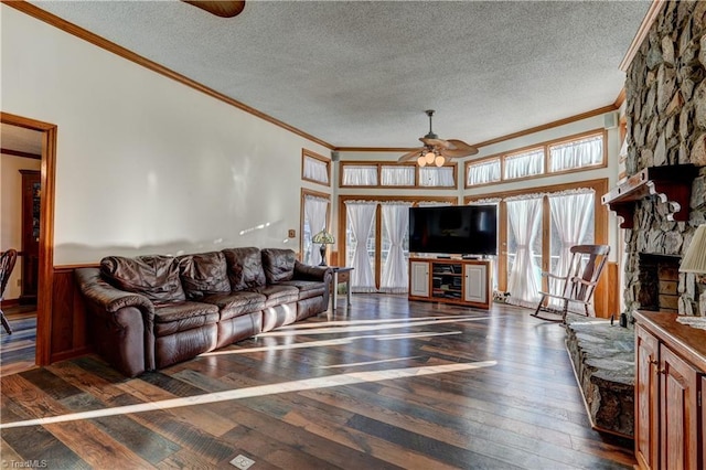 living room with dark hardwood / wood-style flooring, a textured ceiling, ceiling fan, crown molding, and a stone fireplace