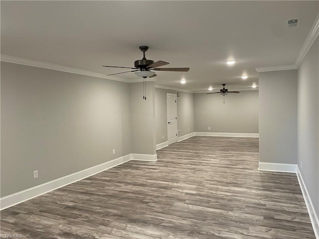 spare room featuring dark wood-style flooring, visible vents, ornamental molding, ceiling fan, and baseboards