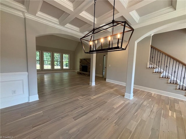 unfurnished living room featuring ornamental molding, wood finished floors, beamed ceiling, stairs, and a fireplace