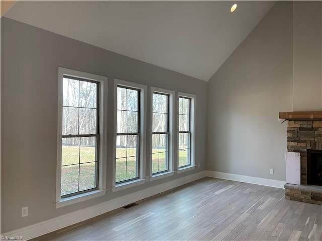 unfurnished living room with visible vents, plenty of natural light, a stone fireplace, and wood finished floors