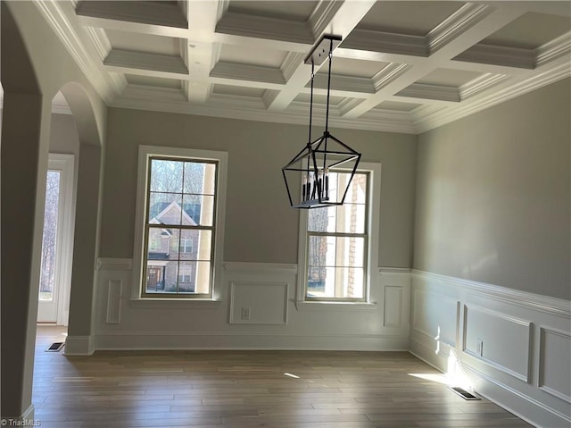 unfurnished dining area featuring arched walkways, a wainscoted wall, hardwood / wood-style floors, beamed ceiling, and a notable chandelier