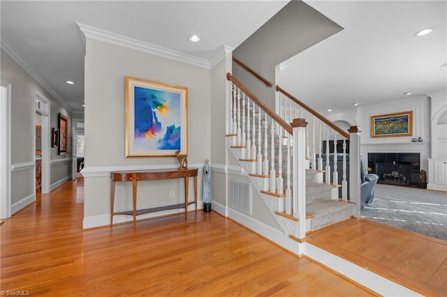 stairway featuring wood-type flooring, a fireplace, and crown molding