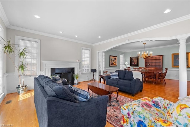 living room with a notable chandelier, light hardwood / wood-style flooring, ornamental molding, and decorative columns