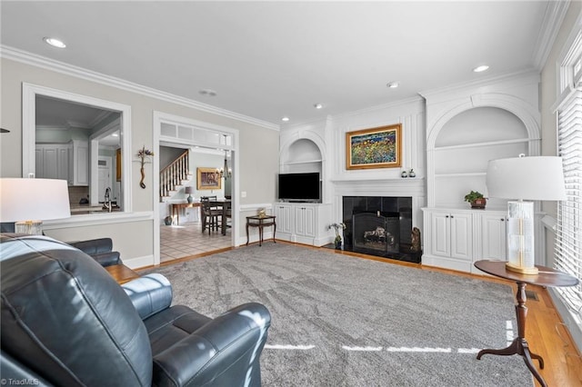 living room with crown molding, built in features, light hardwood / wood-style floors, and a tile fireplace