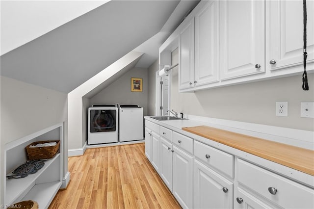 clothes washing area featuring cabinets, sink, washing machine and dryer, and light hardwood / wood-style flooring