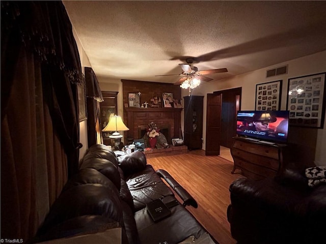 living room with wood-type flooring, ceiling fan, a textured ceiling, and a fireplace