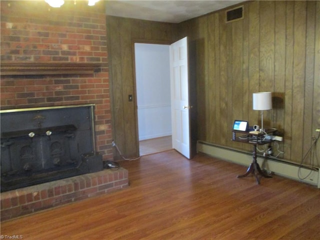 unfurnished living room with visible vents, a fireplace, wooden walls, and wood finished floors