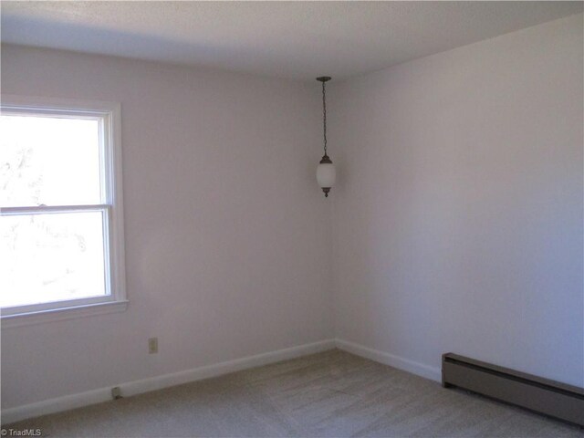 empty room with a baseboard radiator, baseboards, and light carpet