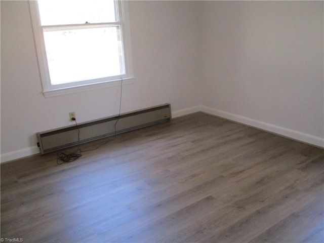 spare room featuring a baseboard heating unit, baseboards, and wood finished floors