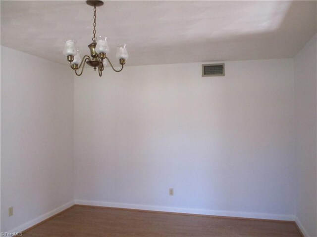 empty room featuring wood finished floors, a notable chandelier, baseboards, and visible vents