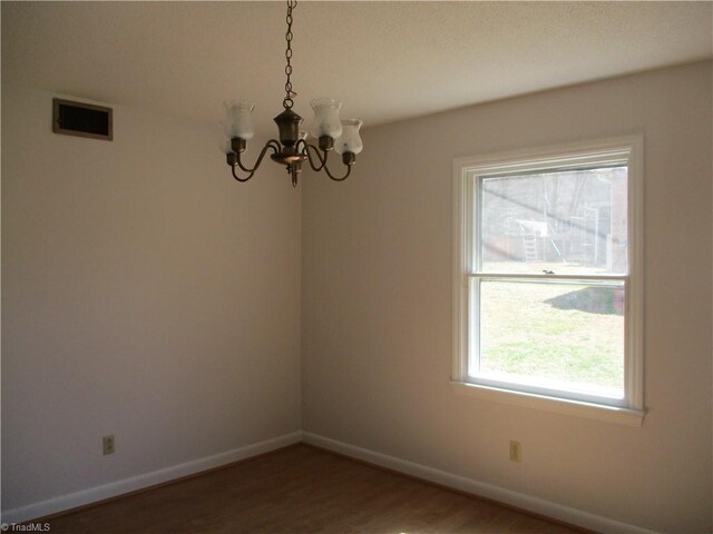 unfurnished room with a notable chandelier, visible vents, baseboards, and wood finished floors