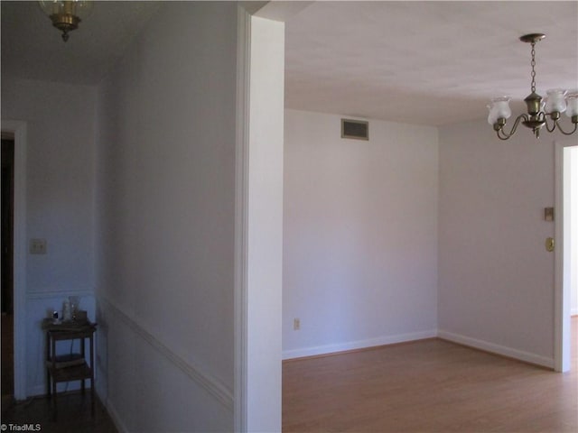 corridor with a notable chandelier, wood finished floors, visible vents, and baseboards