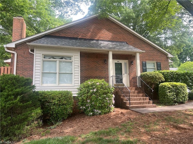 bungalow-style house featuring a chimney, brick siding, and a shingled roof