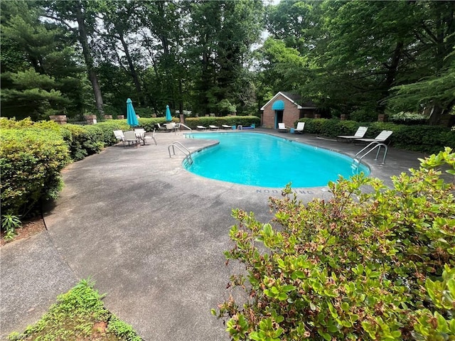 community pool with a patio area, an outdoor structure, and view of scattered trees