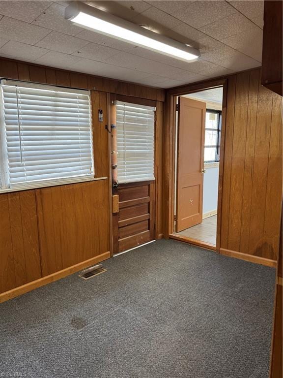 carpeted spare room featuring visible vents, baseboards, and wooden walls