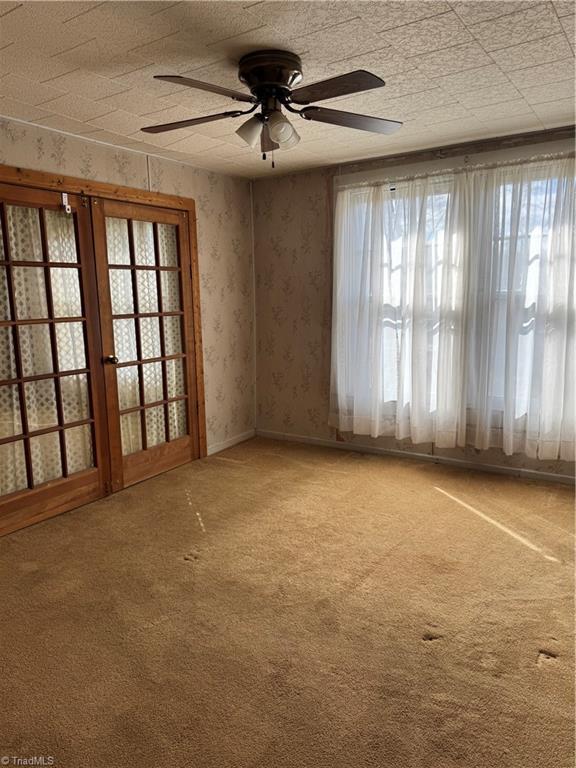 carpeted spare room featuring a wealth of natural light, ceiling fan, and wallpapered walls