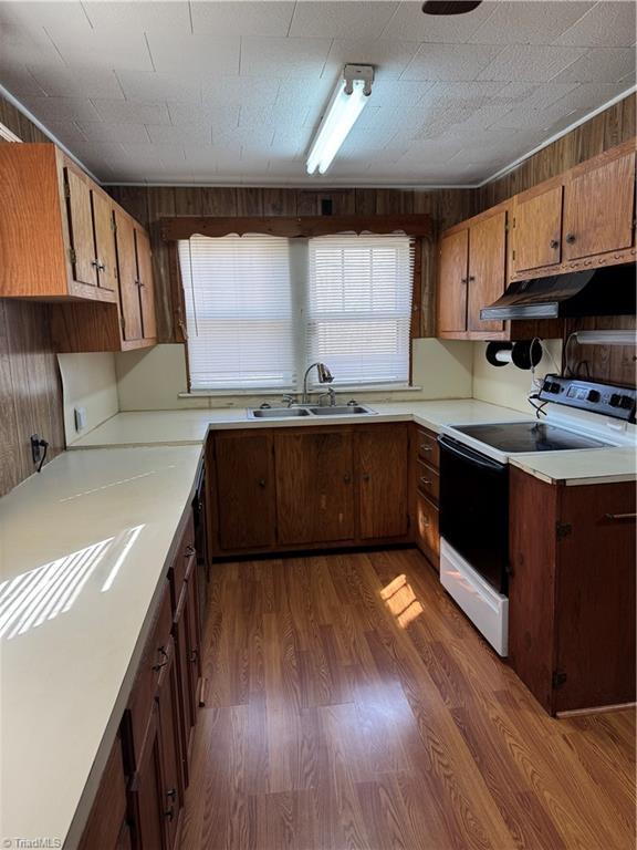 kitchen featuring a sink, under cabinet range hood, light countertops, white range with electric stovetop, and dark wood-style flooring