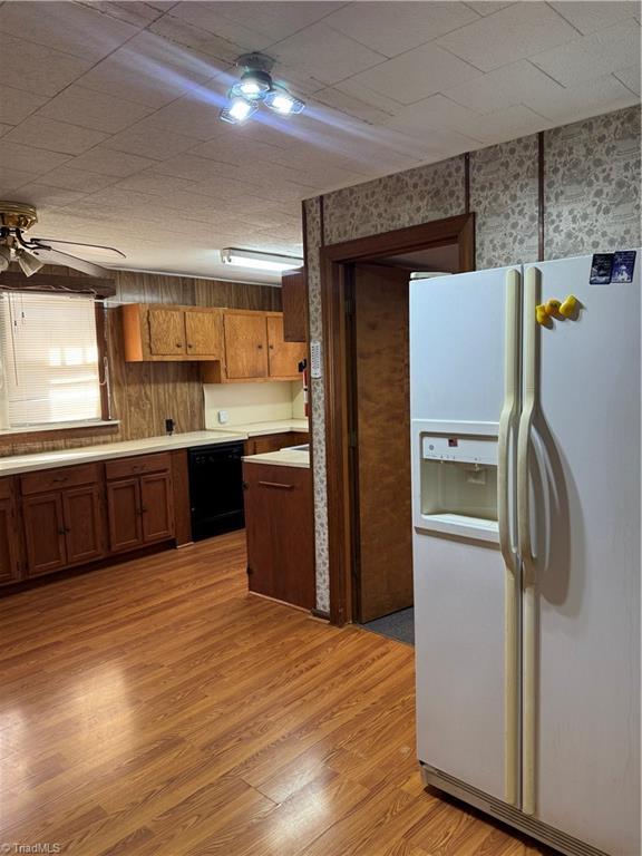 kitchen featuring light wood finished floors, wallpapered walls, white refrigerator with ice dispenser, dishwasher, and brown cabinets