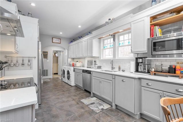 kitchen with arched walkways, independent washer and dryer, range hood, stainless steel appliances, and a sink