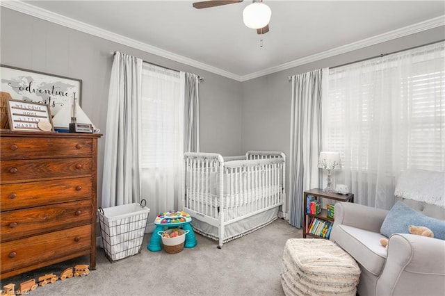 carpeted bedroom with a crib, ornamental molding, and a ceiling fan