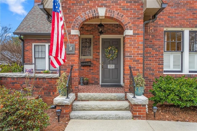 view of exterior entry with brick siding and roof with shingles