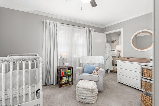 carpeted bedroom with a nursery area, ornamental molding, and a ceiling fan