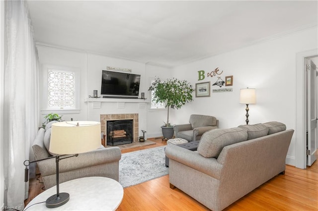 living area featuring a tiled fireplace, light wood-type flooring, and baseboards