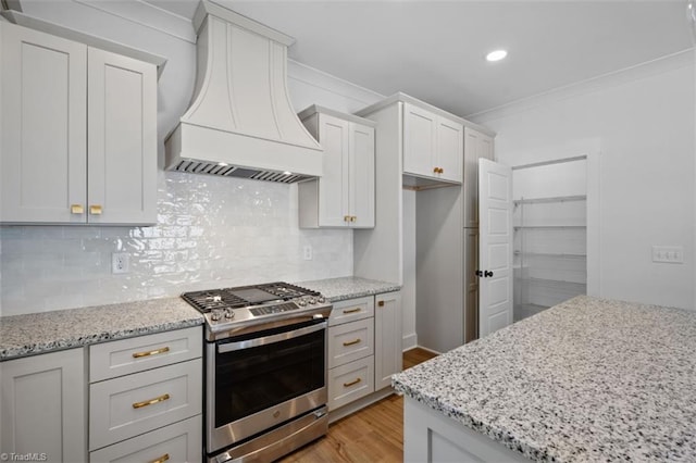 kitchen with light stone counters, light wood-type flooring, decorative backsplash, custom exhaust hood, and gas range