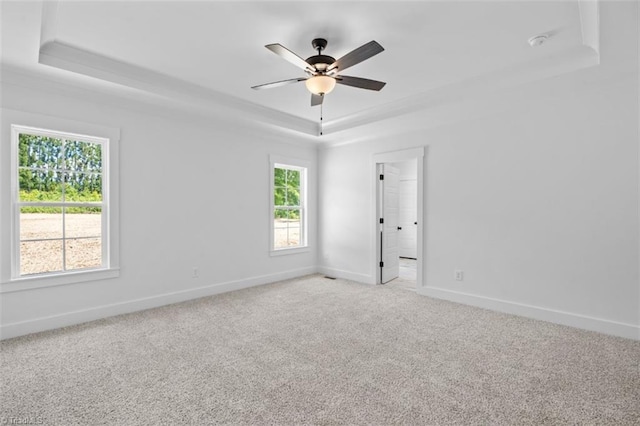 carpeted empty room with ceiling fan, a healthy amount of sunlight, and a raised ceiling