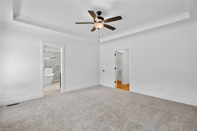 unfurnished bedroom with ensuite bath, light carpet, ceiling fan, and a raised ceiling